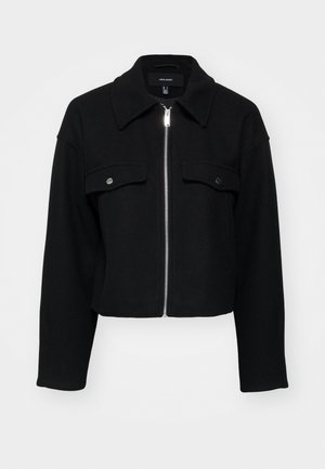 Sagriezta melna jaka, izgatavota no mīksta auduma, ar rāvējslēdzēju priekšā, norādītu apkakli un divām krūšu kabatām ar sudraba pogām.