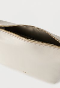 Beežist nahast kotike kuldse luku ja sujuva voodriga seest. Lihtne ristkülikukujuline disain ilma nähtavate mustriteta.