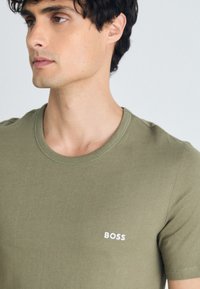 Olivgrünes Baumwoll-T-Shirt mit Rundhalsausschnitt und kleinem weißen "BOSS"-Logo auf der linken Brust. Weiche Textur mit lässigem Schnitt.
