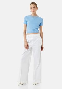 Suéter corto de manga corta en azul claro con un escote adornado con perlas, combinado con pantalones anchos blancos y tacones de punta.