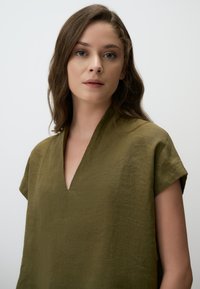 Maglietta corta a maniche corte verde oliva realizzata in un tessuto leggero e testurizzato, con scollatura a V e vestibilità ampia. Design semplice senza motivi.