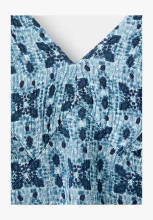 Tissu bleu et bleu canard avec motif floral et à pois bleu foncé, montrant un tissage texturé et un détail de couture en forme de V.