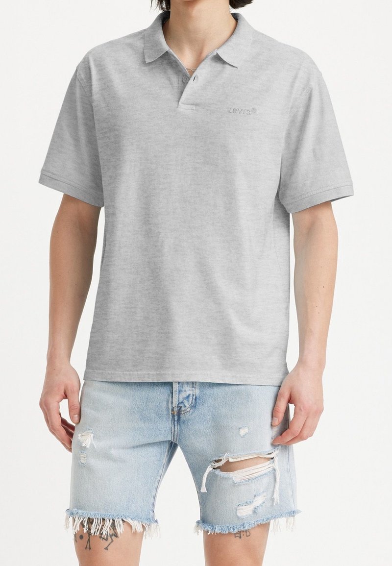 Homme portant un polo gris clair à manches courtes et un short en jean bleu clair usé avec des ourlets effilochés.