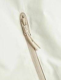 Baltas audinys, artimas planas, kuriame matomas užtrauktukas su tekstūruotu smėlio spalvos traukikliu, akcentuojantis lygią medžiagą ir sustiprintą siūlę palei užtrauktuko kraštą.