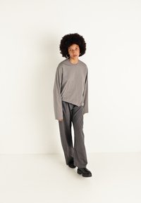 Grijze lange mouwen top met een relaxte pasvorm, gecombineerd met verticaal gestreepte wijde broek in zwart en grijs, en chunky zwarte schoenen.