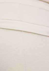 Crèmekleurige gebreide stof met een textuurafwerking en een opgevouwen tailleband, voorzien van subtiele stikdetails en een overall gladde uitstraling.