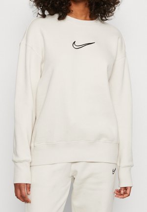 Crèmekleurige sweatshirt gemaakt van zachte stof. Bevat een zwart geborduurd Nike-logo op de borst en ribbelboorden en -zoom.