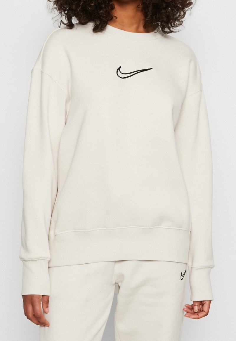 Krämfärgad sweatshirt i mjukt tyg. Har en svart broderad Nike-logotyp på bröstet samt ribbade muddar och fåll.