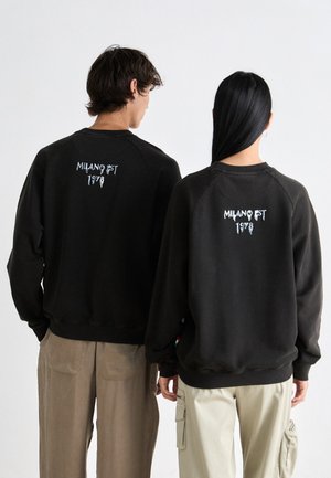 Sorte sweatshirts med raglanærmer og ribbede kanter har "MILANO FST 1978" i hvid broderi på ryggen. Materialet synes at være blødt.