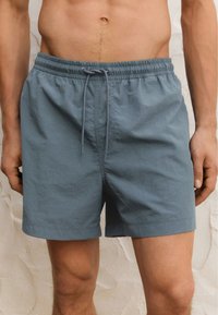 Pantaloni da nuoto da uomo in tessuto azzurro chiaro, con vita elasticizzata e cordino, caratterizzati da un design semplice e una superficie liscia.