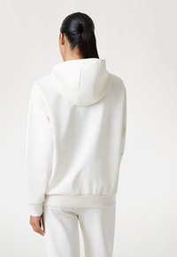 Witte katoenen hoodie met een ruime capuchon, geribde boorden en zoom, en een gladde textuur. Gepaarde met bijpassende lichtgekleurde broek.