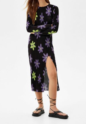 Sort ribbet kjole med lange ærmer, der har store lilla og grønne blomster mønstre, sideslids, parret med sorte strappy sandaler.