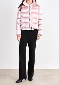 Lyserød pufferjakke med vandrette kamre, lynlåslukning og høj krave. Kombineret med sorte bukser med vide ben og sorte spidse hæle.