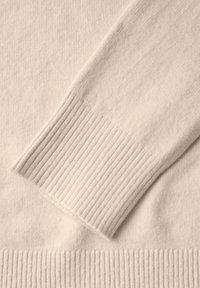 Pull léger beige avec une texture douce, doté de bordures côtelées aux poignets et à l'ourlet. Le matériau semble lisse et tricoté, avec de subtiles variations de teinte.