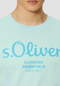 Light blue t-shirt made of cotton, featuring bold "s.Oliver" logo and text. Crew neck design, smooth texture, and casual style.