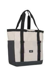 Tote taška v béžovej a čiernej farbe, vyrobená z pevnej tkaniny, s dvojitými čiernymi uchami a obdĺžnikovým telom s nálepkou na prednej strane.