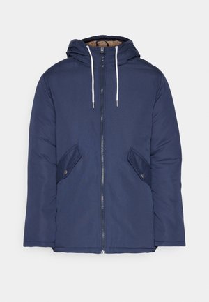 Veste matelassée bleu marine avec capuche, dotée d'une fermeture éclair à l'avant, de deux poches latérales avec boutons et de cordons de serrage blancs.