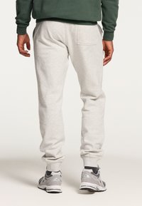 Sivé tepláky vyrobené z mäkkého materiálu, so slim-fit strihom a zúženou nohou, s vreckom na zadnej strane a rebrovanými manžetami. Nosené so sivými teniskami.