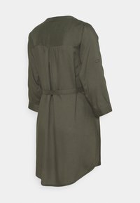 Vue de dos d'une robe vert olive mi-longue avec manches trois-quarts, une ceinture étroite et un tissu froncé sous le yoke.