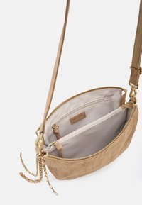 Borsa a tracolla in pelle beige chiaro con finitura testurizzata, tasche interne e accessori in metallo color oro. Presenta una tracolla lunga regolabile e chiusura con cerniera.