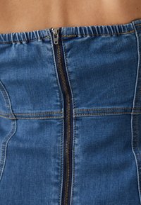 Μπλε τζιν κορσέ με δομημένο σχέδιο, διαθέτοντας κλείσιμο με φερμουάρ YKK και αντίθετη χρυσή ραφή κατά μήκος των ραφών.