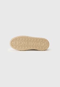 Semelle de sneaker couleur crème avec caoutchouc texturé, comportant des lettres en relief et des motifs d'étoiles. Forme arrondie, conçue pour l'adhérence et le confort.
