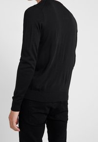 Svart stickad tröja med långa ärmar, ribbade muddar och nederkant, med en enkel rund nacke och en mjuk yta.