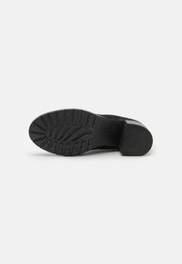 Suola di scarpa nera con motivo di battistrada testurizzato, tacco in gomma piatto e design sagomato per presa e stabilità. Finitura liscia senza segni.