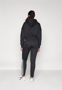 Sweatshirt preta com um design cropped e cintura elástica, combinada com calças pretas ajustadas com riscas brancas laterais. Ténis brancos.