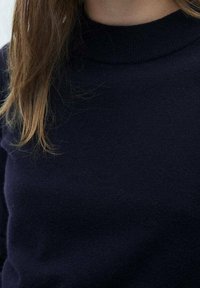 Marineblauwe, gebreide trui met een hoge hals. Zachte textuur met een aansluitend ontwerp, voor een deel bedekt door lang, steil haar.