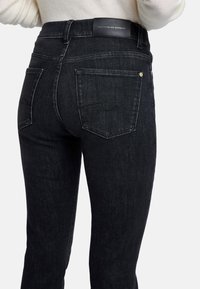Jean en denim noir taille haute à coupe droite. Comprend deux poches arrière et une étiquette en cuir au dos de la taille. Texture lisse.