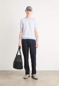 Maglione corto a maniche corte di colore azzurro chiaro con polsini a contrasto, pantaloni blu navy, berretto grigio e borsa nera. Le scarpe scamosciate completano l'outfit.