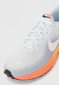 Jasnoniebieski but sportowy z teksturowaną siateczką na górze, białym logo Nike, pomarańczową i szaro-skalistą podeszwą oraz białymi sznurowadłami.