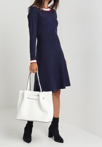 Navy dress with red and white striped neckline, knee-length skirt, paired with a white tote bag featuring a flat handle and a minimalist design.