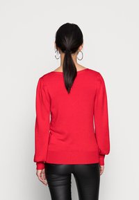 Roter Pullover mit langen Puffärmeln, weitem Ausschnitt und geripptem Saum. Hergestellt aus weichem Strickmaterial mit glatter Textur.