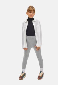 Leggings grises combinadas con un suéter de cuello alto negro y una camisa blanca con botones, complementadas con zapatillas deportivas multicolores y calcetines blancos.