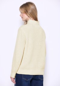 Maglione lavorato a maglia di un giallo chiaro con colletto alto, texture a coste e maniche lunghe. Design senza cuciture con una vestibilità rilassata. Nessun motivo distintivo.