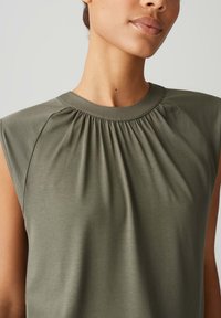 Olive green sleeveless top with gathered neckline and soft texture, featuring a round collar and a relaxed fit.