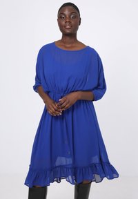 Blauwe jurk tot de knie met een strakke taille, ronde halslijn en driekwart mouwen. Heeft een ruffled zoom en lichte stof.