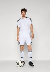 Wit Adidas voetbaluniform met zwarte strepen, bestaande uit een shirt met ronde hals, korte broek en knielange sokken. Zwarte voetbalschoenen en een voetbalk bal met patroon.
