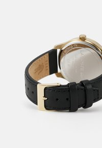 Correa de reloj de cuero negro con hebilla y acentos en tono dorado, presenta un fondo de acero inoxidable con detalles grabados.