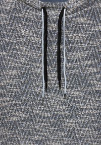 Kapuzensweatshirt mit Fischgrätenmuster in Blau und Weiß, mit schwarzen und hellblauen Kordeln und Metallspitzen. Strukturiertem Stoff.