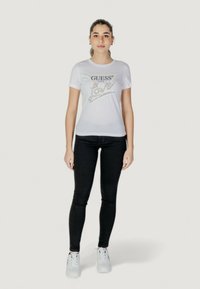 Witte katoenen t-shirt met "GUESS USA Love" graphic in zilver, gecombineerd met zwarte skinny jeans en witte sneakers. Eenvoudig, aansluitend ontwerp.
