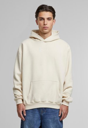 Crème kleurige hoodie van zacht materiaal, met een voorzak, ribbenboorden en een geborduurd logo. Casual pasvorm met een ontspannen ontwerp.