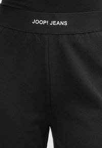 Calças de jogging pretas com cós elástico, apresentando o logótipo branco "JOOP! JEANS", feitas de tecido suave com um acabamento ligeiramente texturizado.