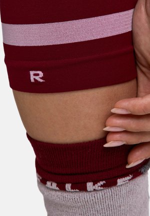 Chaussette de sport bordeaux arrivant au genou avec des rayures roses. Présente une texture côtelée au niveau de la bordure et la lettre "R" en rose sur le côté.