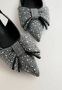 Garozenie ar norādītu purngalu, kas izgatavoti no melna materiāla ar sudrabainām rhinestones, dekorēti ar dekoratīvu loku uz katras kurpes.