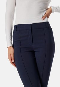 Marineblauwe op maat gemaakte broek met een gladde textuur, voorzien van een aangesloten taille en subtiele kreukdetails aan de voorkant. Ontworpen voor een gestroomlijnde uitstraling.