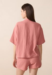 Laza szabású, textúrált rózsaszín felső és shorts szett, rövid ujjal és gallérral, könnyű anyagból készült, hátulról látható.
