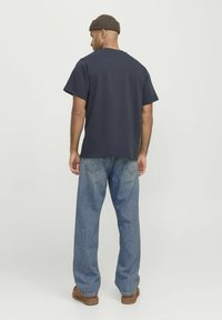 Dunkelblaues Kurzarmhemd mit lockerem Schnitt, kombiniert mit hellblauen weiten Jeans und braunen Slippern. Weicher Baumwollstoff.